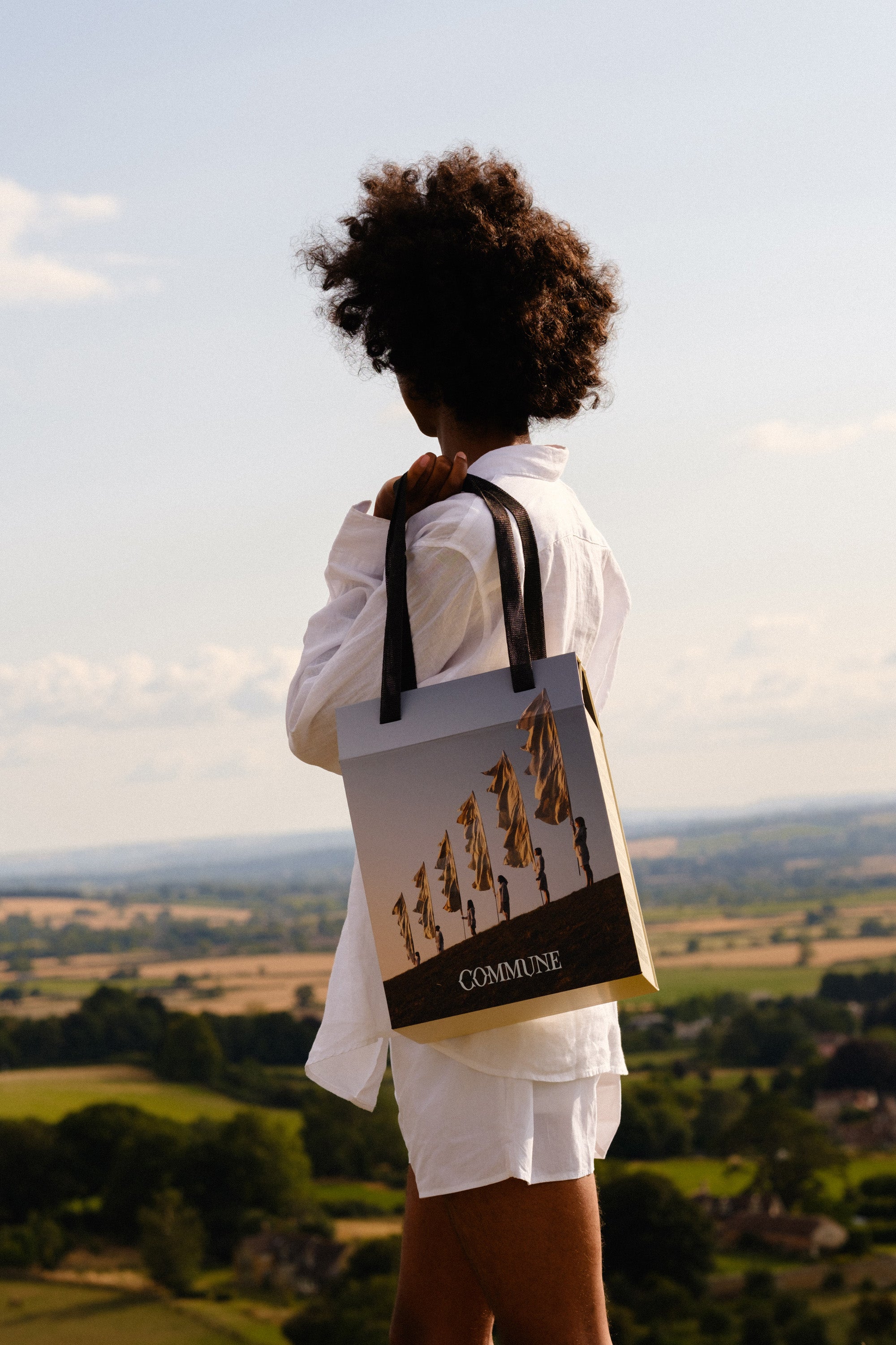 Person holding Commune's signature Seymour Collection box including 6 sustainable body care products against a scenic landscape