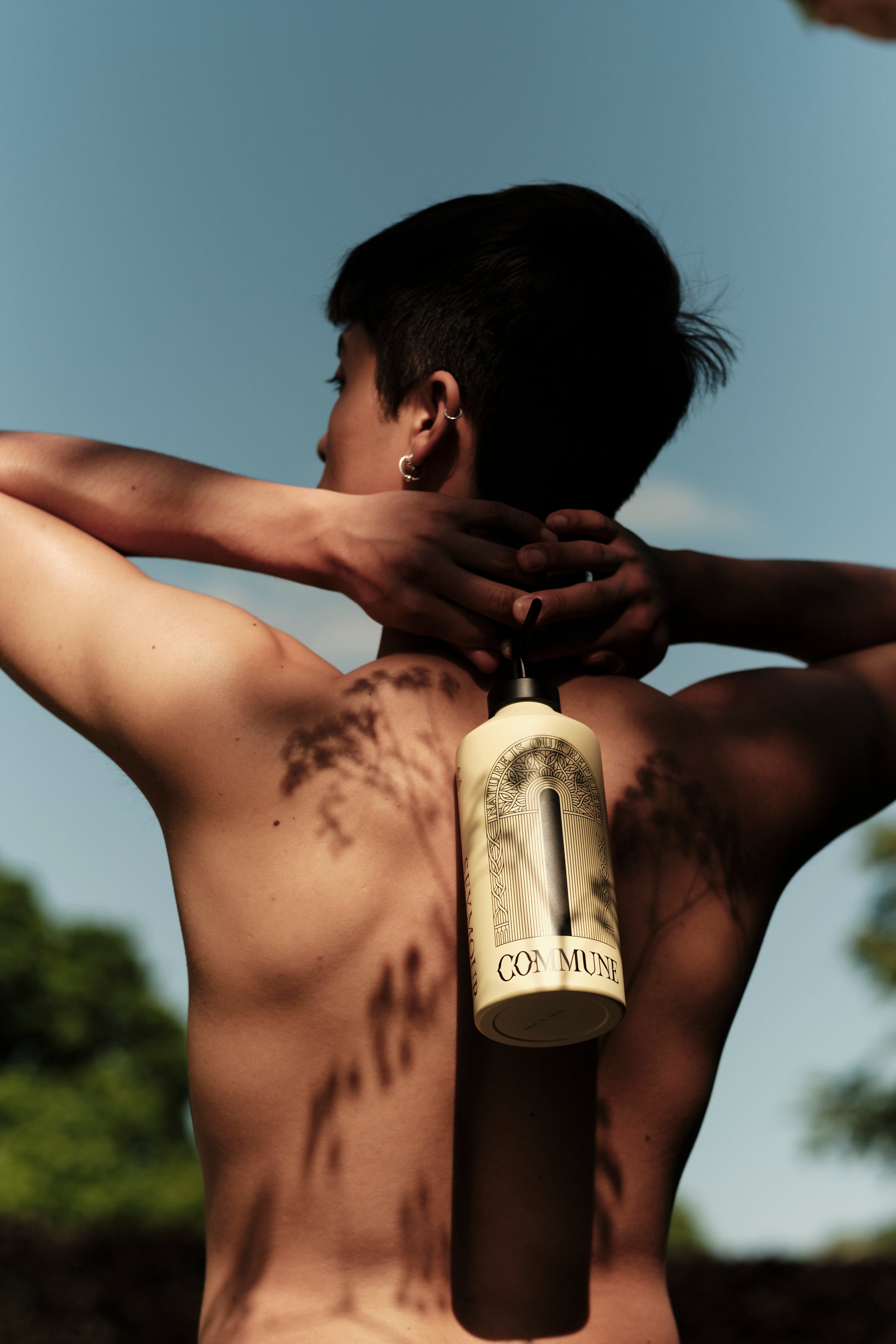 Person holding a bottle of Commune luxury body wash against a natural background