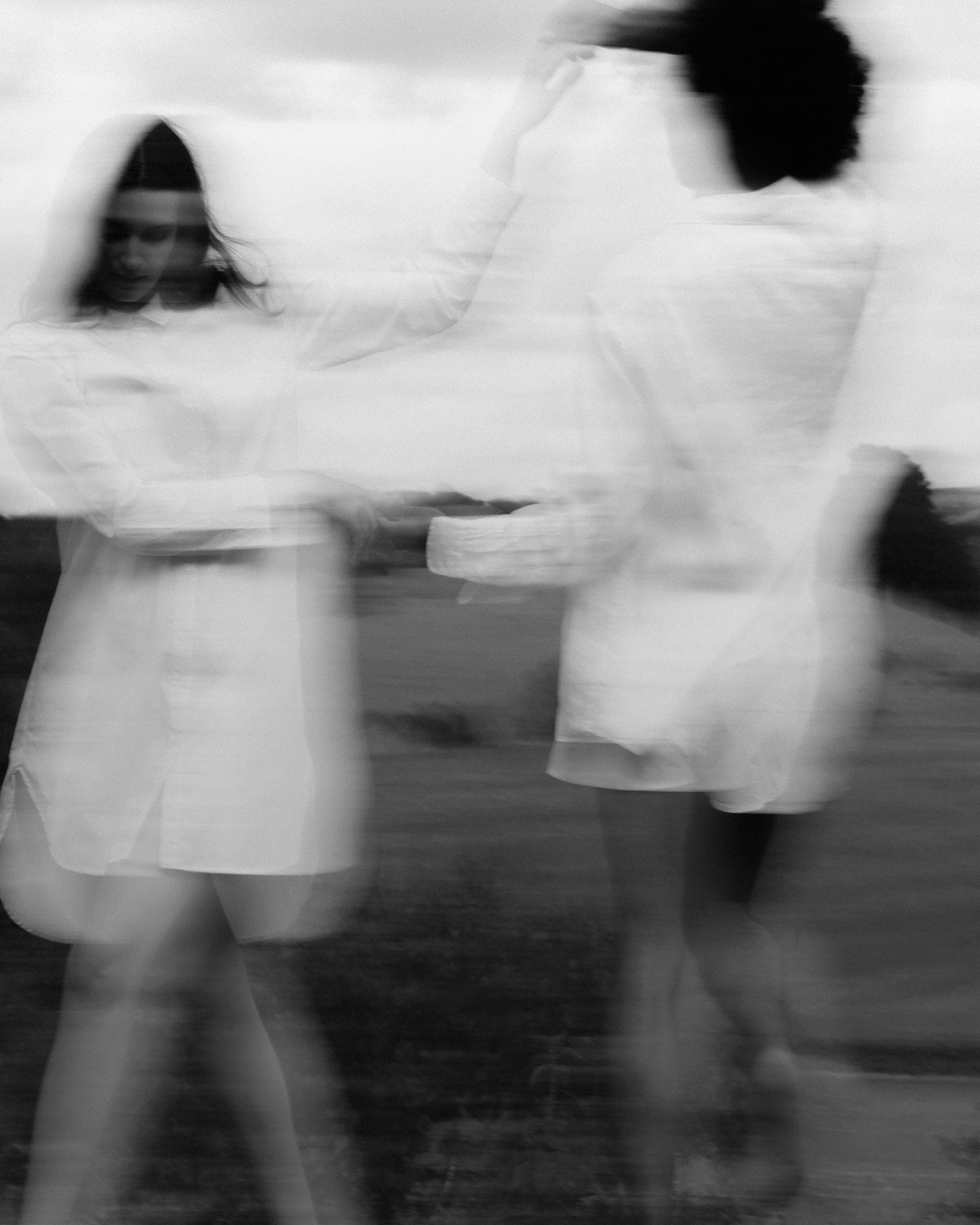 Two people holding hands with a blurred effect, standing on a grassy field.